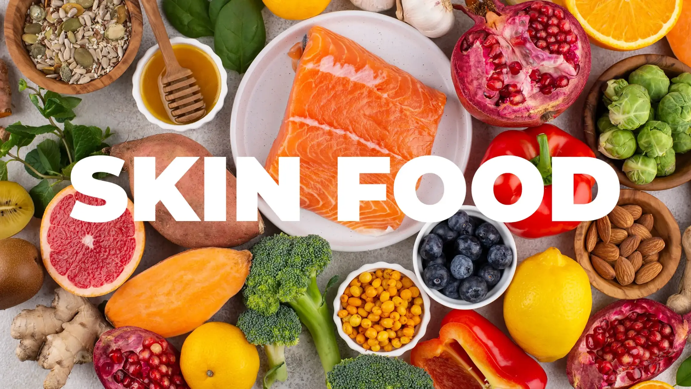 A vibrant overhead layout of skin-boosting foods including salmon, broccoli, sweet potatoes, blueberries, and almonds with the text Skin Food.