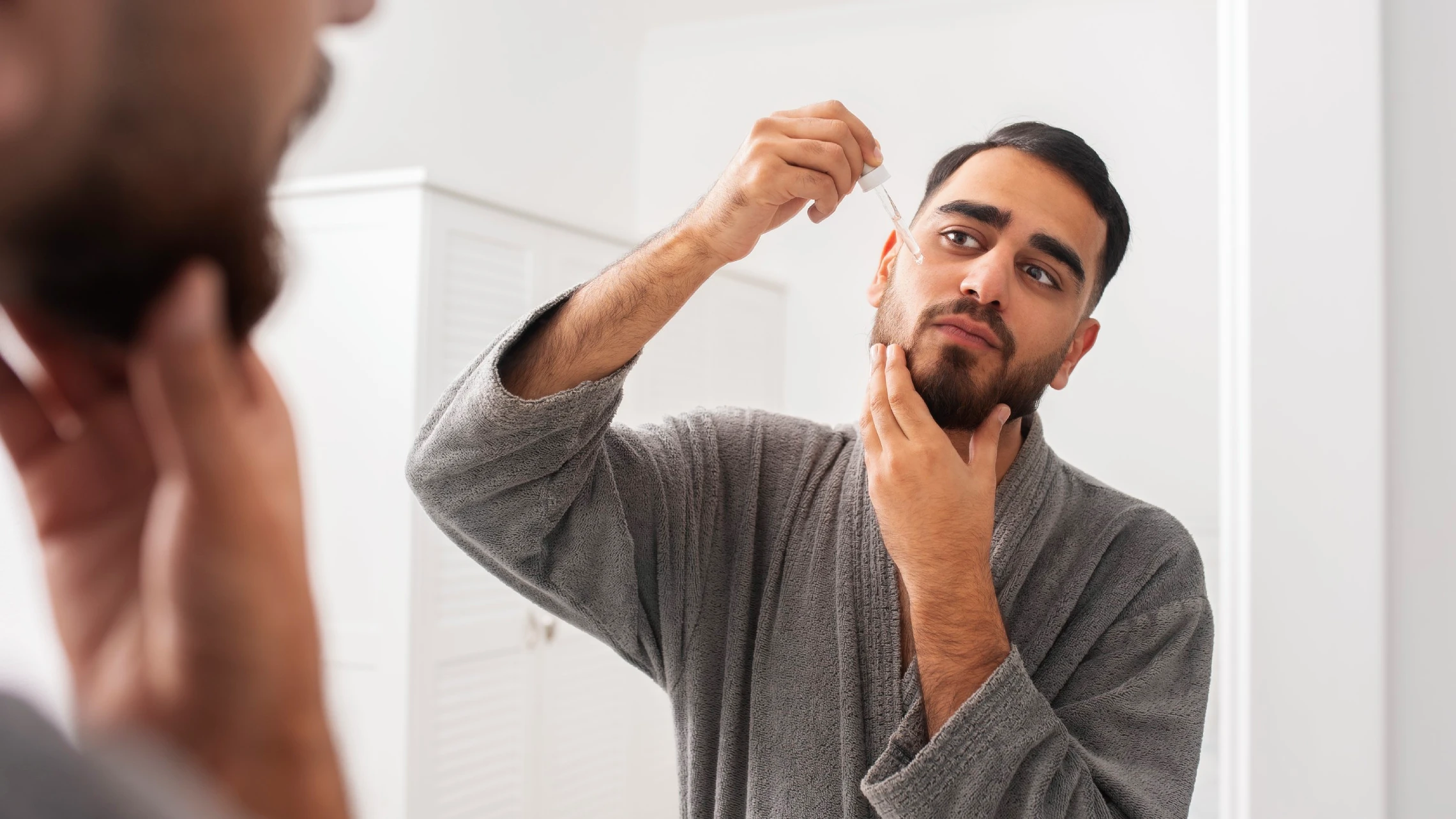 closeup of a man applying serum to his skin looking in a mirror to protect his skin barrier from damage