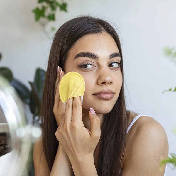 closeup of a young woman cleansing her face with a cloth as part of her good skincare routine for acne and oily skin