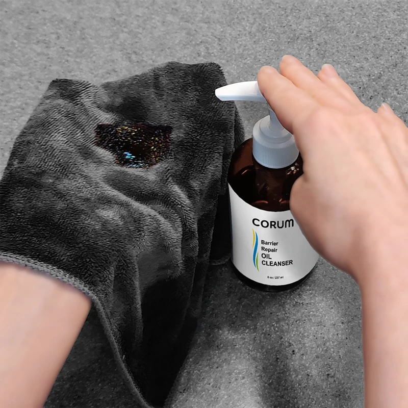 woman's hand pumping Corum Oil Cleanser onto a cloth