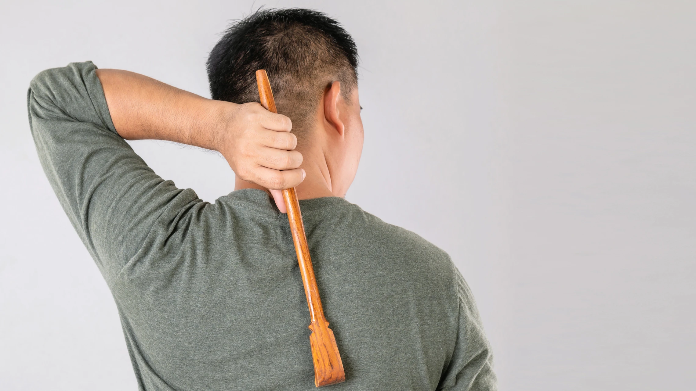 Man scratching his dry, itchy back with a wooden backscratcher