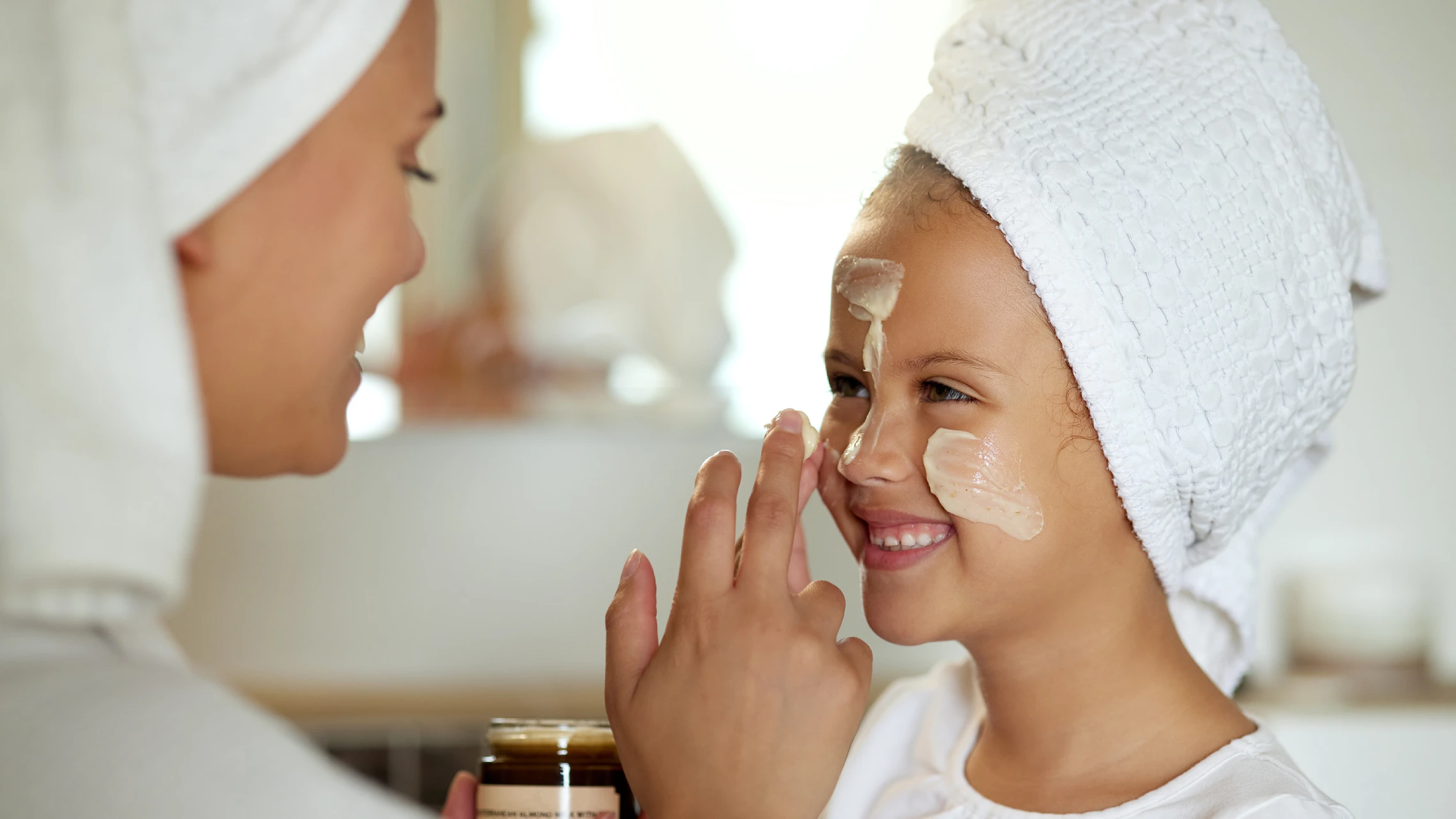 A mother gently applying a fragrance-free cream to her toddler's arm after a bath.
