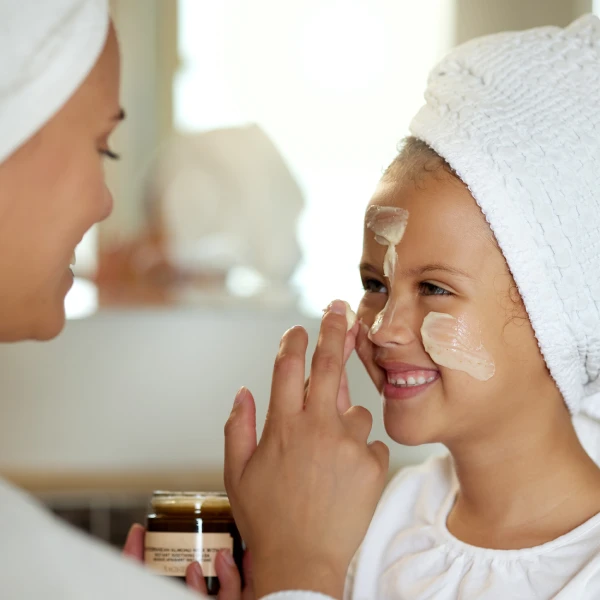 A mother gently applying a fragrance-free cream to her toddler's arm after a bath.