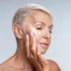 thoughtful-mature-woman-applying-cream-moisturizer-to-face