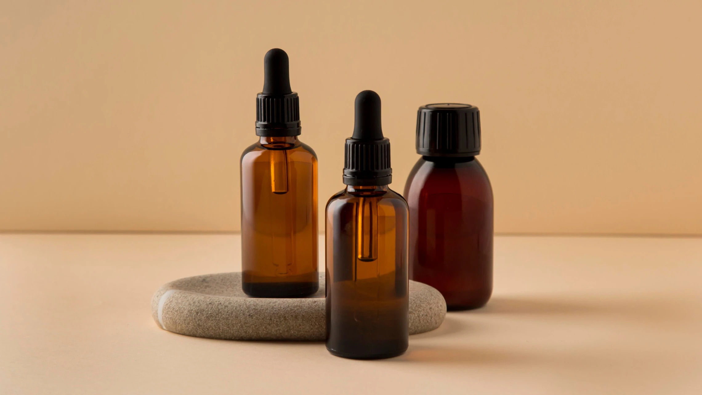 Three amber glass dropper bottles with minimalist skincare oils on a neutral beige background.