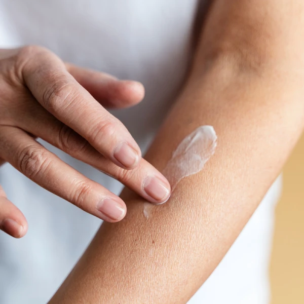A person applying a small amount of lotion to their inner forearm to patch test a new skincare product for allergic reactions.
