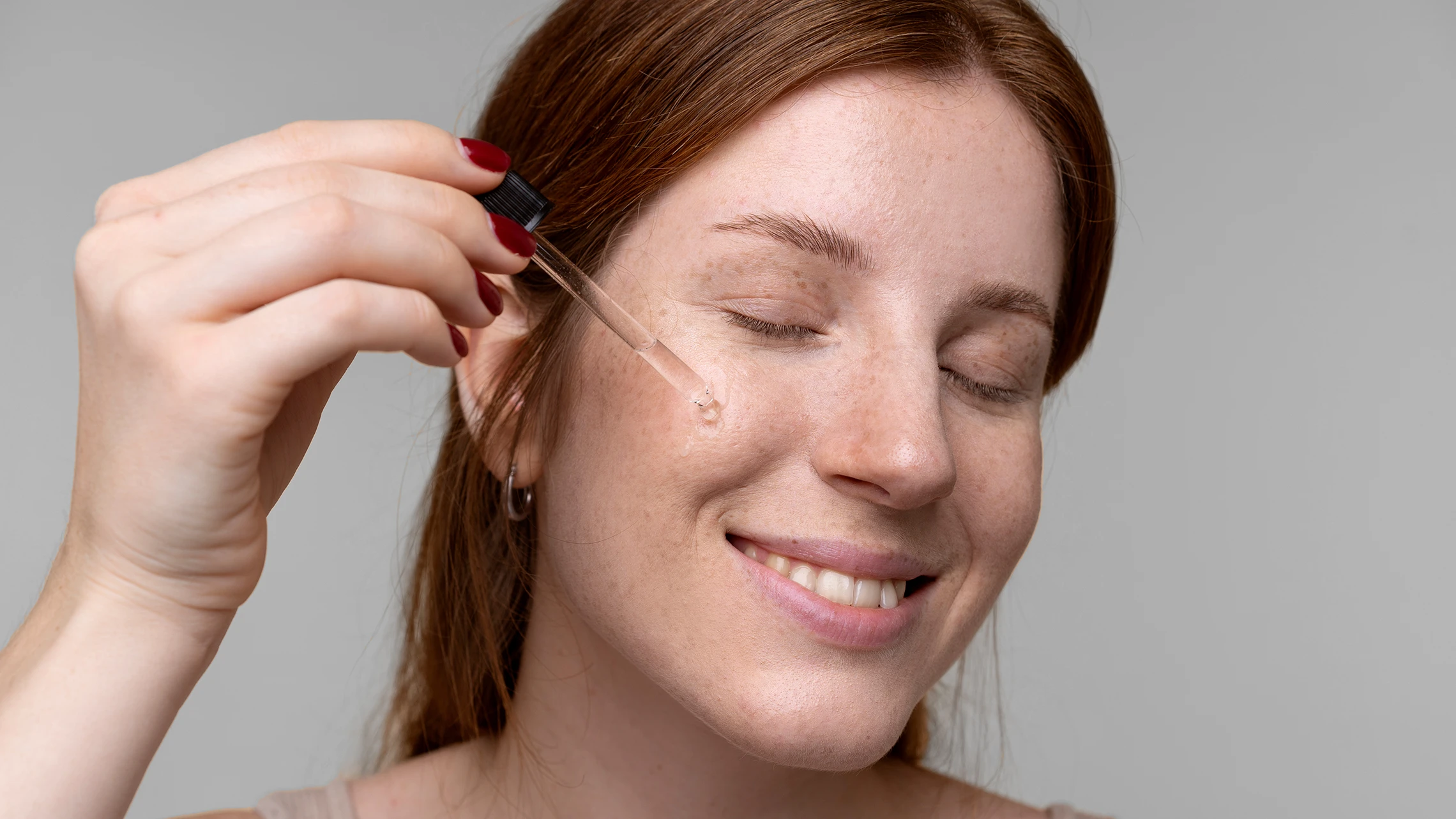 A redhead putting face oil serum on her face and smiling - Can Plant Oils Help Repair the Skin Barrier?