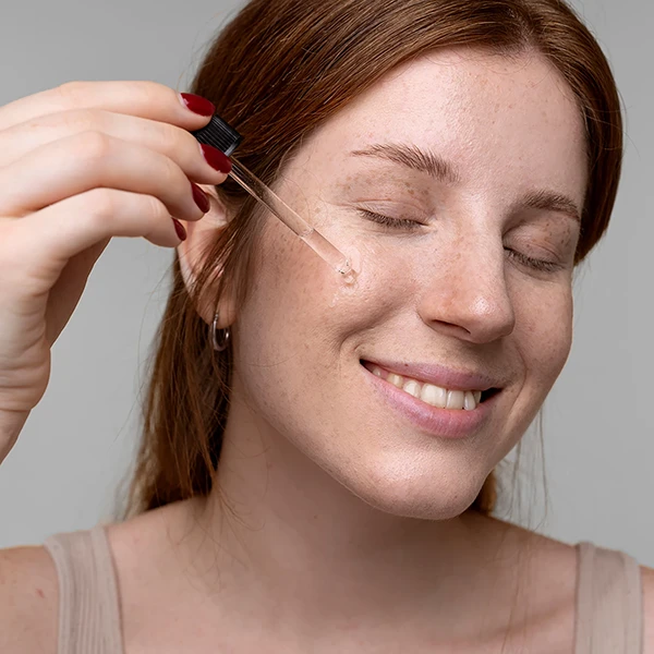 A redhead putting plant oils on her face and smiling