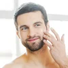 skin-care-handsome-young--man-applying-corum-super-serum-his-face-looking-himself-with-smile-while-standing-front-mirror